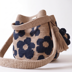 Vista laterale completa della borsa a secchiello all'uncinetto, che mostra la sua forma voluminosa, il motivo floreale bianco e la tracolla posizionata in un anello, con nappe e charm visibili sul lato.